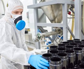 Sports nutrition production worker in protective clothing taking empty container from stack.