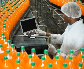 High angle view of male worker using laptop amidst production line in juice factory