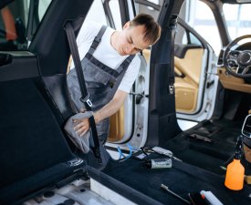 Worker with rag wipes car interior plastic, dry cleaning and detailing. Vehicle washing in garage, thoroughly care of automobile, chemical and vacuum clean service
